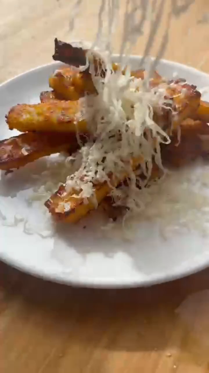 Assiette blanche de frites de polenta dorées et croustillantes, recouvertes d'une pluie de comté fraîchement râpé