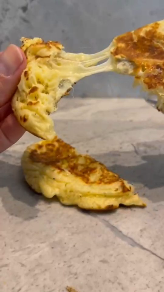 Pancakes salés dorés fourrés au fromage, un pancake soulevé à la main révélant un cœur de fromage fondant qui file