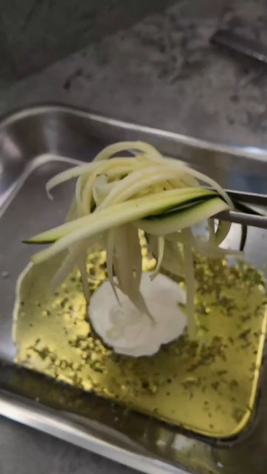 Spaghettis de courgettes crues taillés à la mandoline, soulevés à la pince au-dessus d'un lit de yaourt grec et d'huile d'olive aux herbes