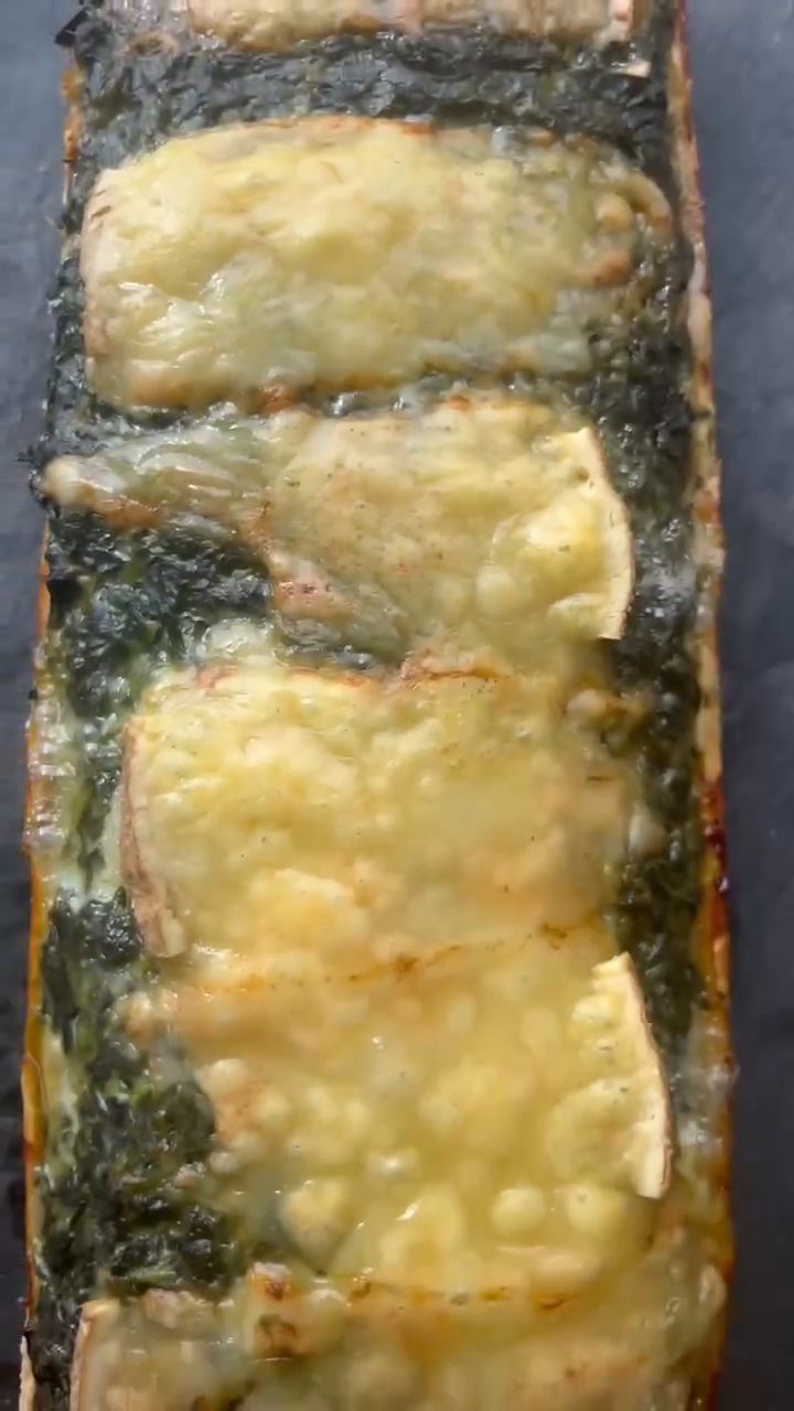 Tarte rectangulaire aux épinards vue du dessus, garniture verte crémeuse recouverte de larges tranches de raclette fumée gratinées et dorées au four